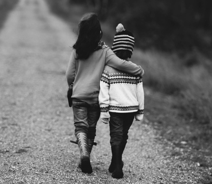 Two children walking down a gravel road, one with an arm around the other